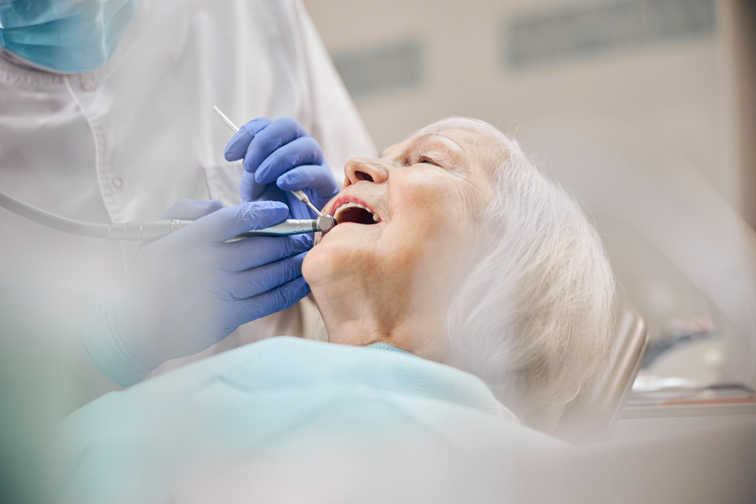 Dentist treating woman patient using drill on her teeth